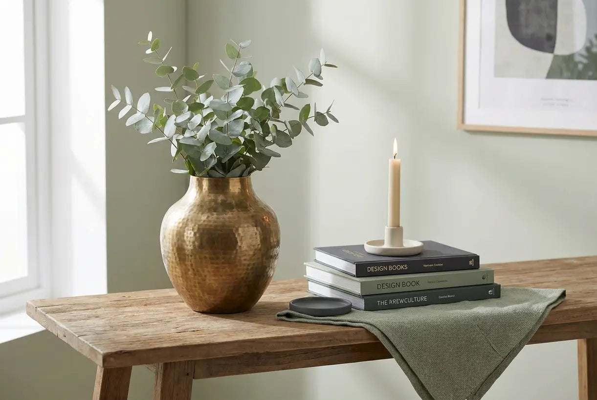 Styled console tabletop with brass flower vase, design books, and botanicals in warm natural light