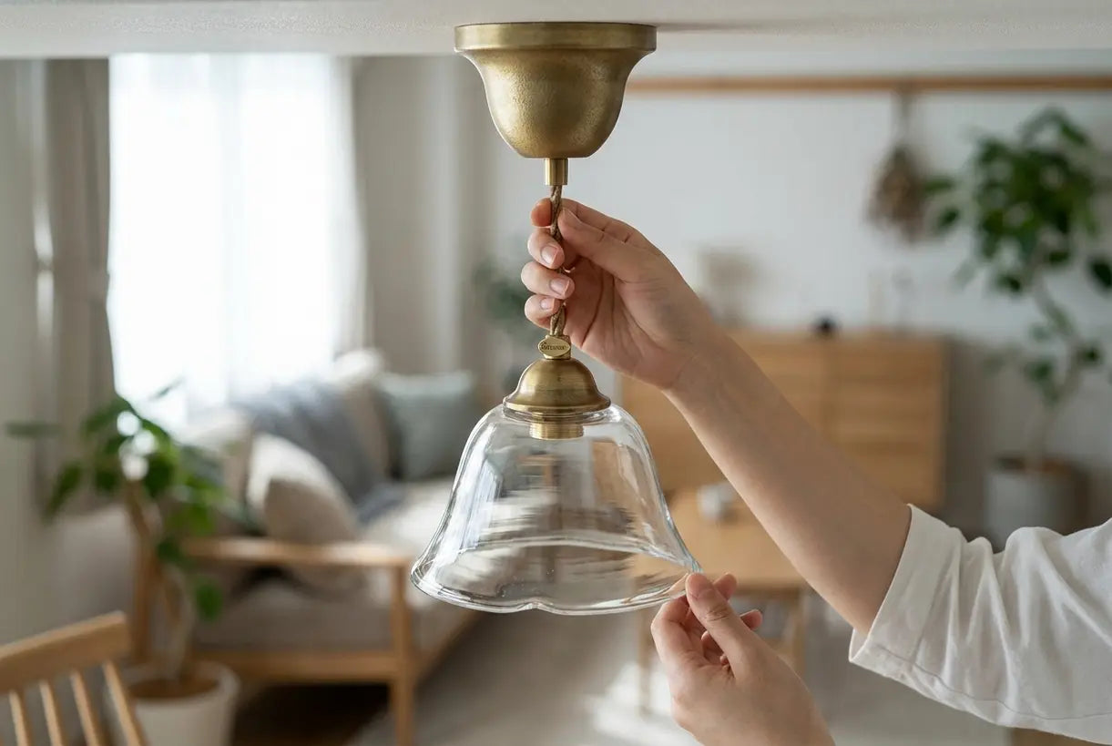 Handen die messing klokvormige hanglamp aanpassen met elegante uitlopende glazen kap