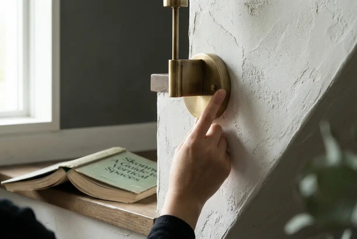 Hand installing brass wall sconce on stairway wall in Scandinavian home