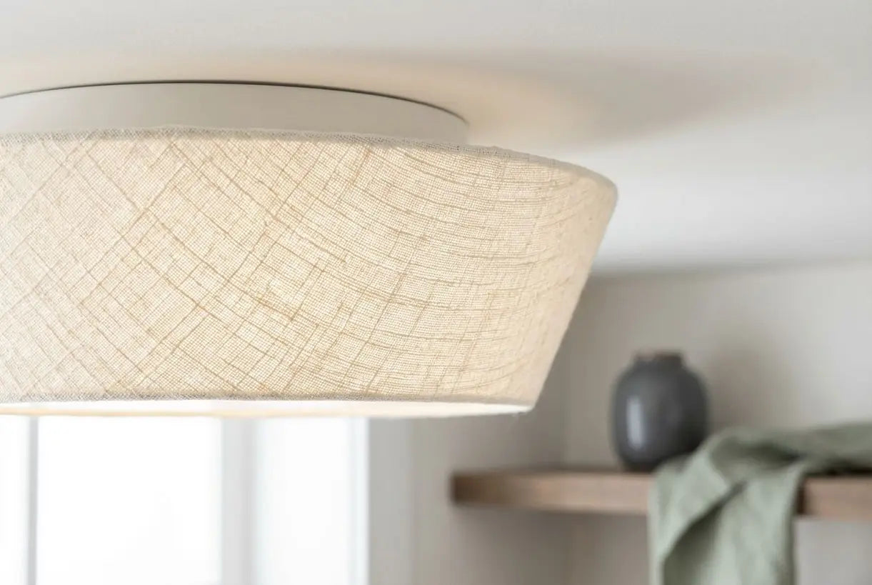 Close-up van de crèmekleurige stoffen kap van een plafondlamp voor vlakke montage, met Scandinavische ambachtelijke details voor een minimalistisch interieur