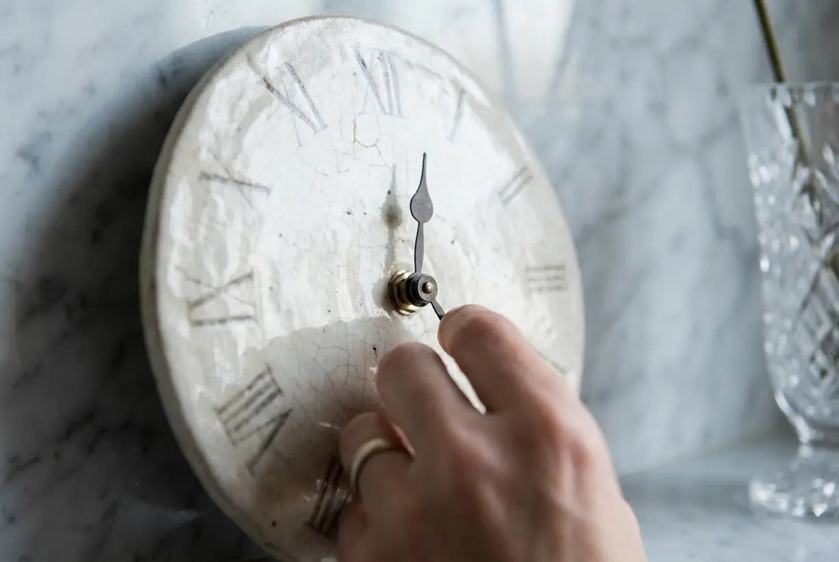 Hands adjusting handcrafted ceramic wall clock face with natural glaze texture