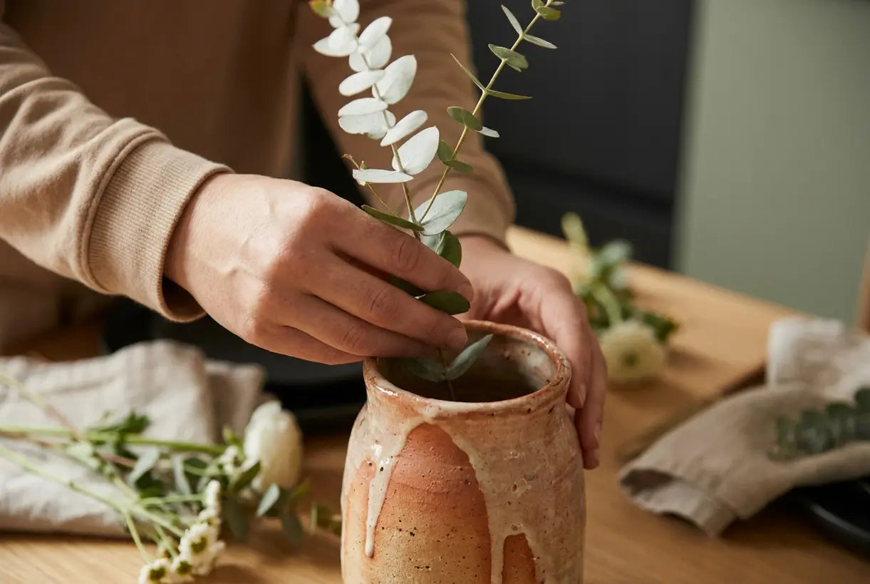 Close-up of hands arranging fresh flowers in a rustic ceramic dining table flower vase, showcasing texture and craftsmanship