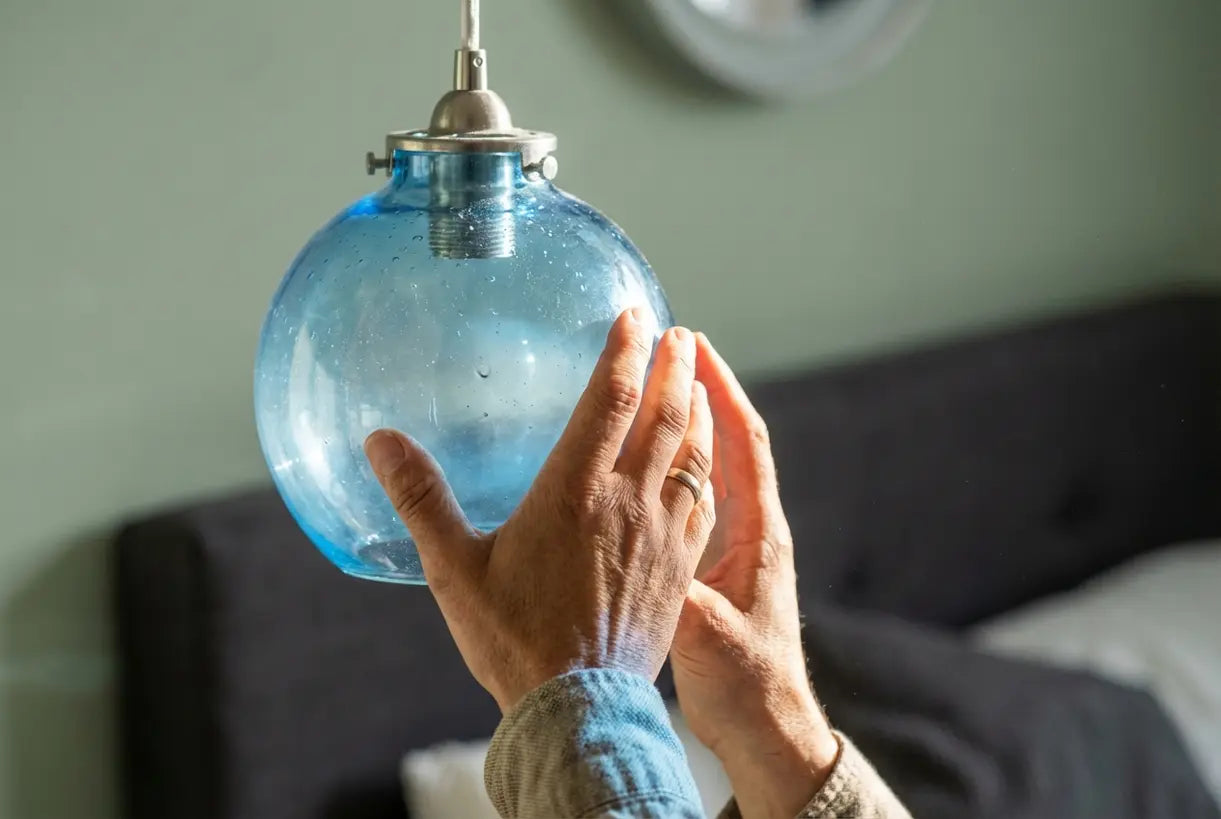Blue glass pendant light detail with hands, calming bedroom lighting design