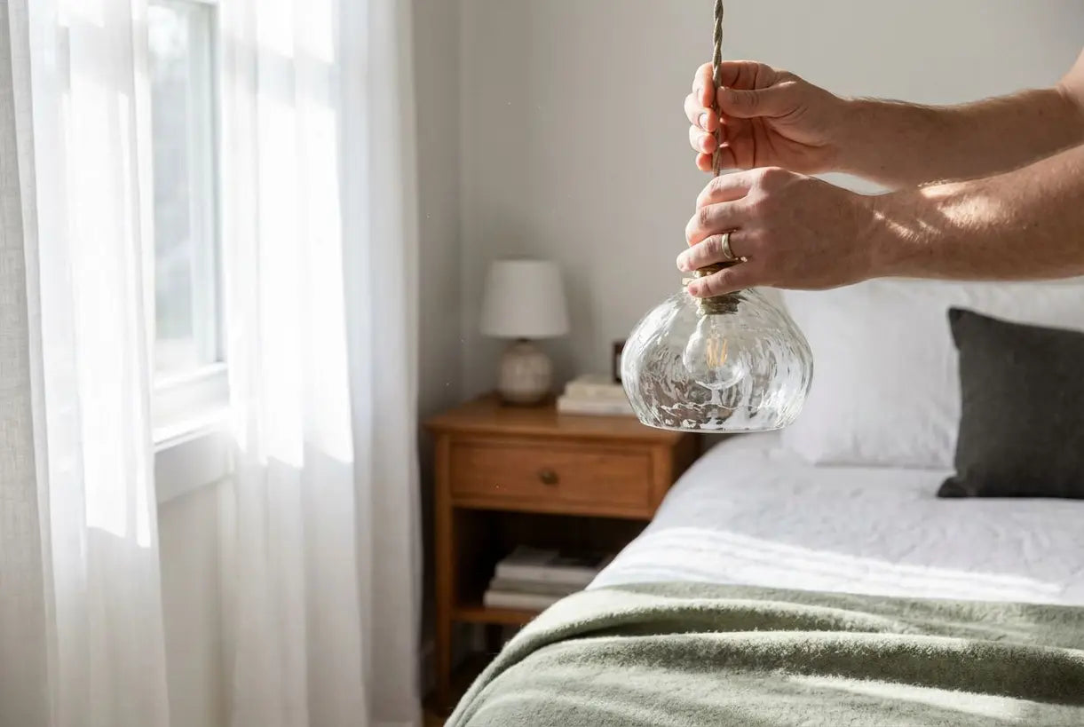 Handen die een glazen hanglamp aanpassen in een Scandinavische slaapkamer plafondverlichting opstelling