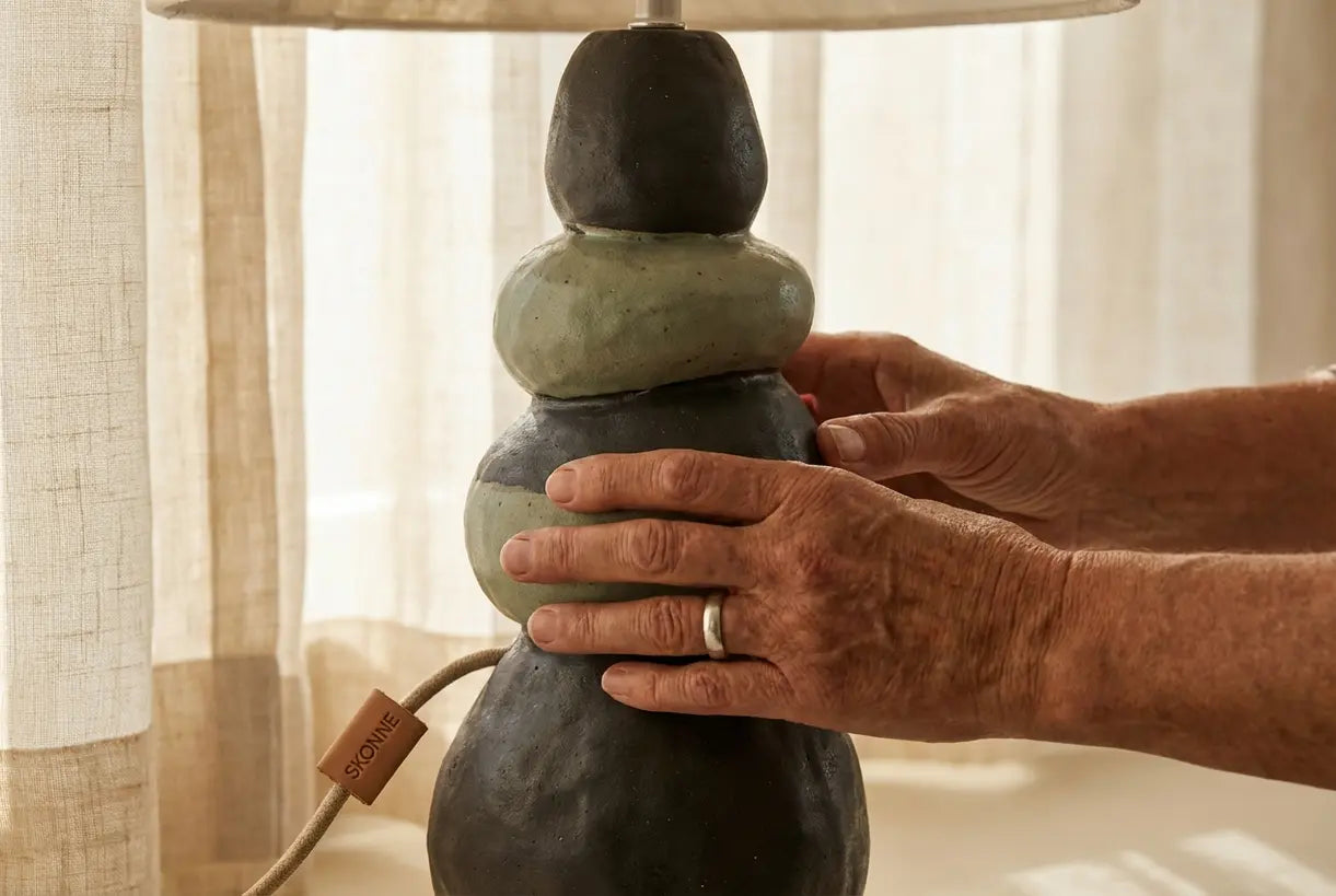 Handen passen de sculpturale keramische tafellampvoet aan met organische textuur en warme natuurlijke verlichting.